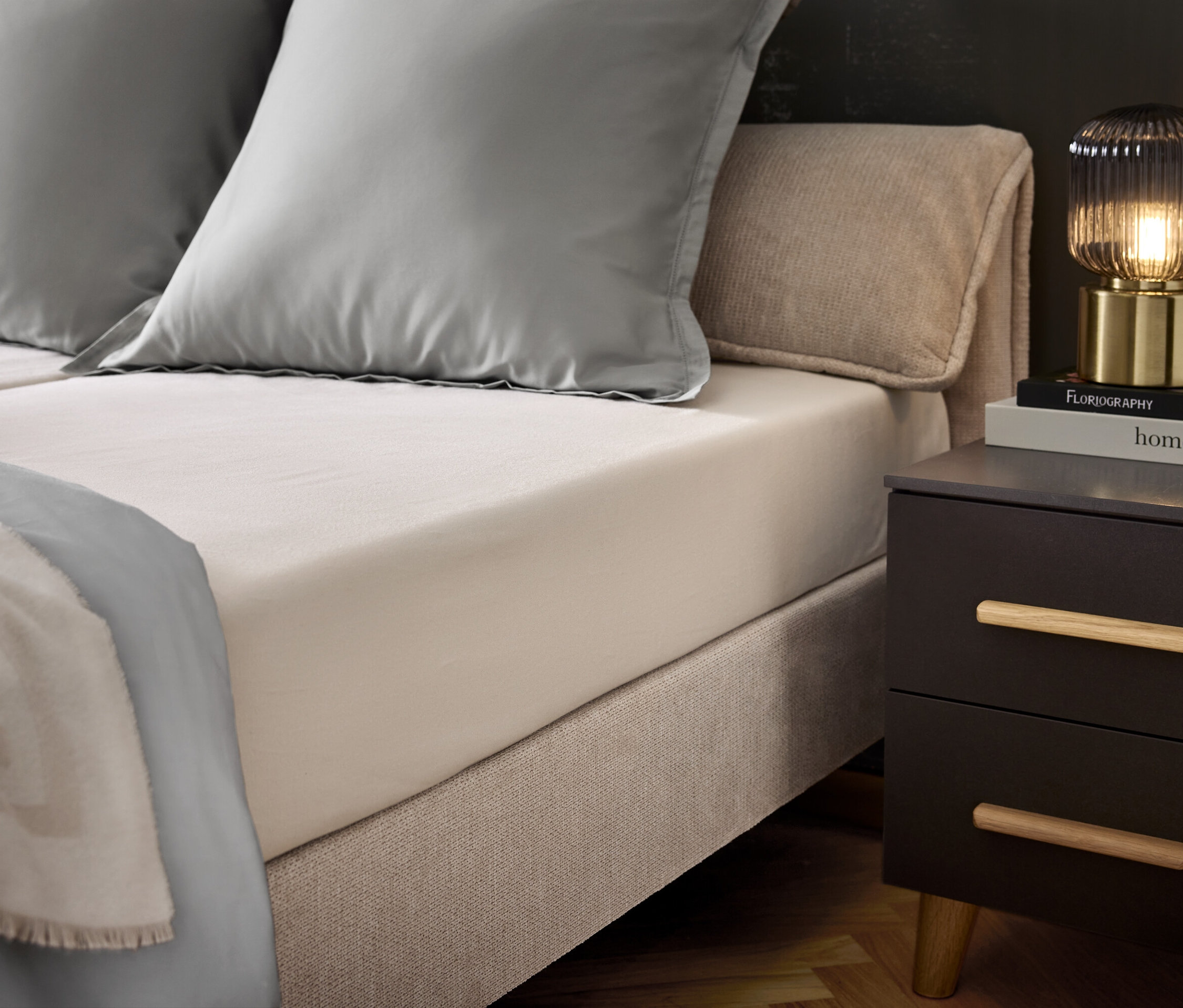 Hálószoba ággyal, két szürke párnával és egy szürke ágytakaróval. Az éjjeliszekrényen egy lámpa és könyvek találhatók.