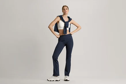 Frau posiert mit Sweatjacke in Navy um die Schultern, weißem Seamless-Sport-Bustier und marineblauer Bodyforming-Sporthose.