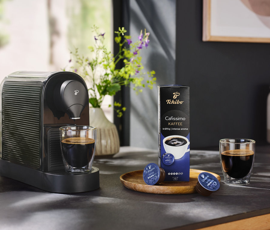 Fekete Cafissimo pure+ kávéfőző egy csésze kávéval és egy csomag kávékapszulával.