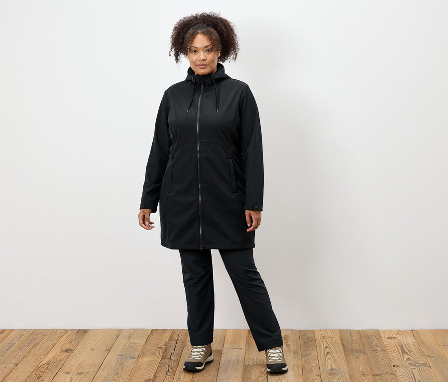 Fekete kabátos és nadrágos nő áll a fapadlón.