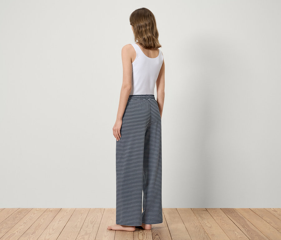Egy nő háttal áll, fehér felsőt és kék csíkos nadrágot visel.