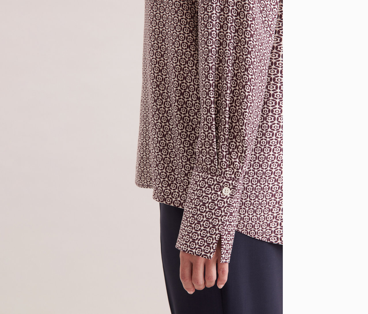 Egy nő közeli képe, aki ekrü-bordó mintás Seidensticker viszkóz tunikát visel.
