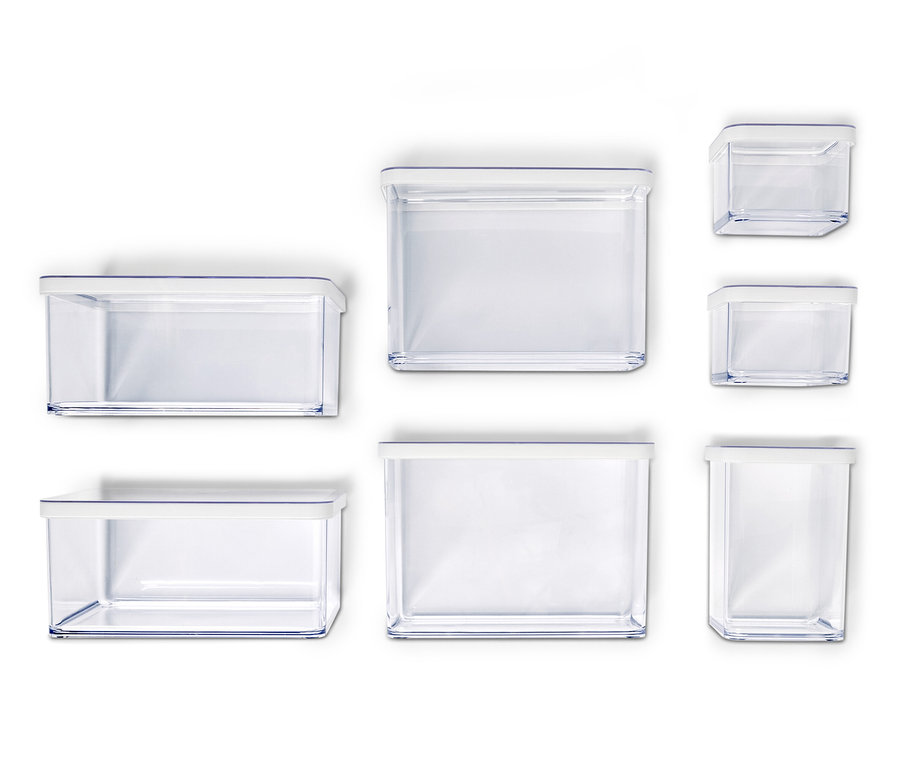 Hét üres, átlátszó tárolóedény fehér fedőkkel, különböző méretekben, fehér háttér előtt elrendezve.