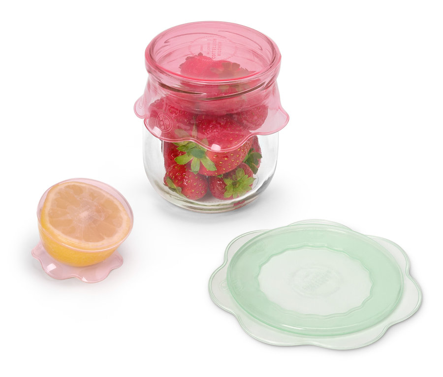 Egy üveg eper rózsaszín fedővel egy fél citrom mellett áll rózsaszín fedővel és egy zöld fedővel.