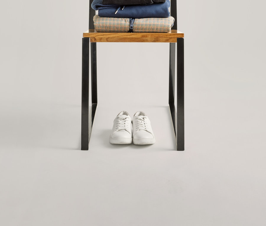 Egy sötétkék táska van egy székre rakott ruhakupacon, köztük egy zöld csíkos, félhosszú ujjú felső és fehér tornacipők.