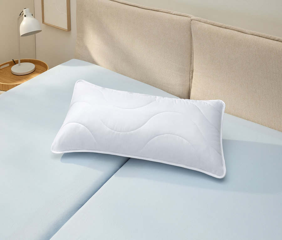 Egy fehér, kifőzhető párna (kb. 80 x 40) fekszik egy világoskék lepedőn.