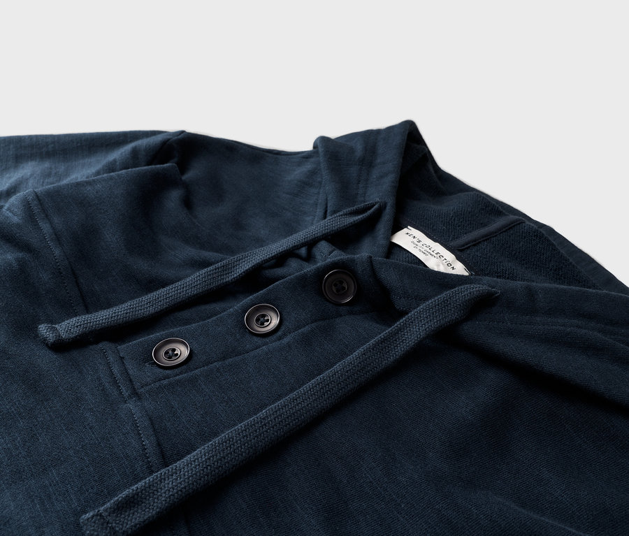 Egy sötétkék, hosszú ujjú ing közeli képe, három gombbal és húzózsinórral.