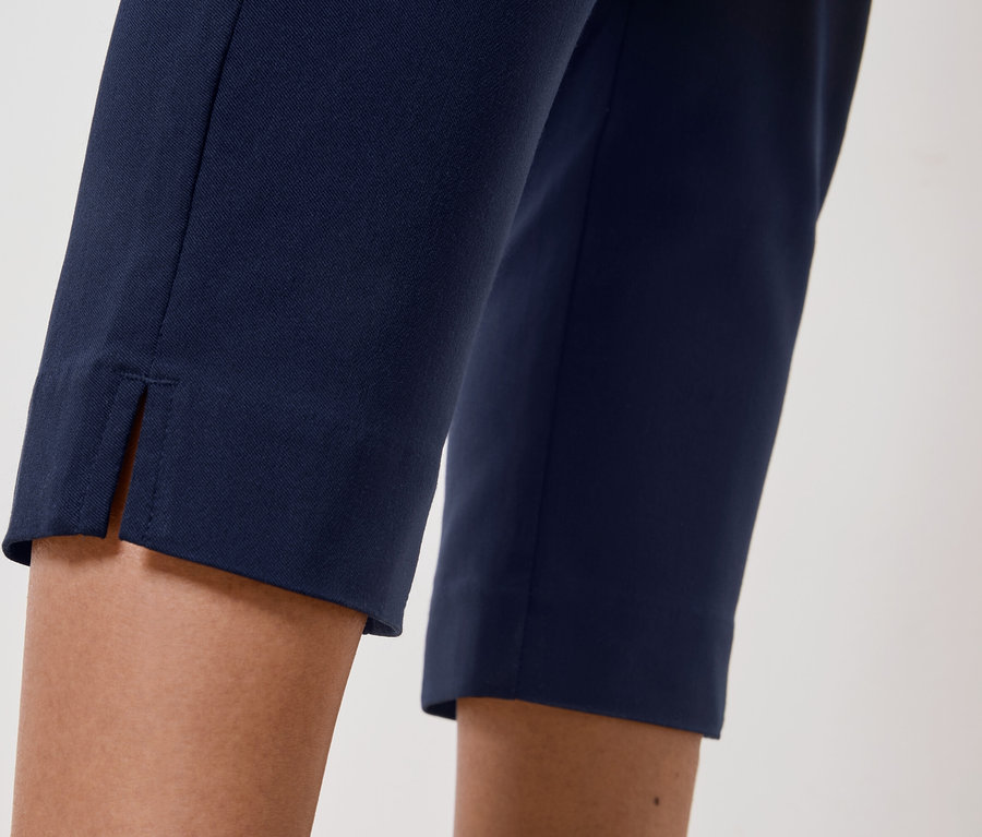 Közeli kép egy személy lábáról, aki tengerészkék nadrágot visel, melynek szegélyén hasíték található.