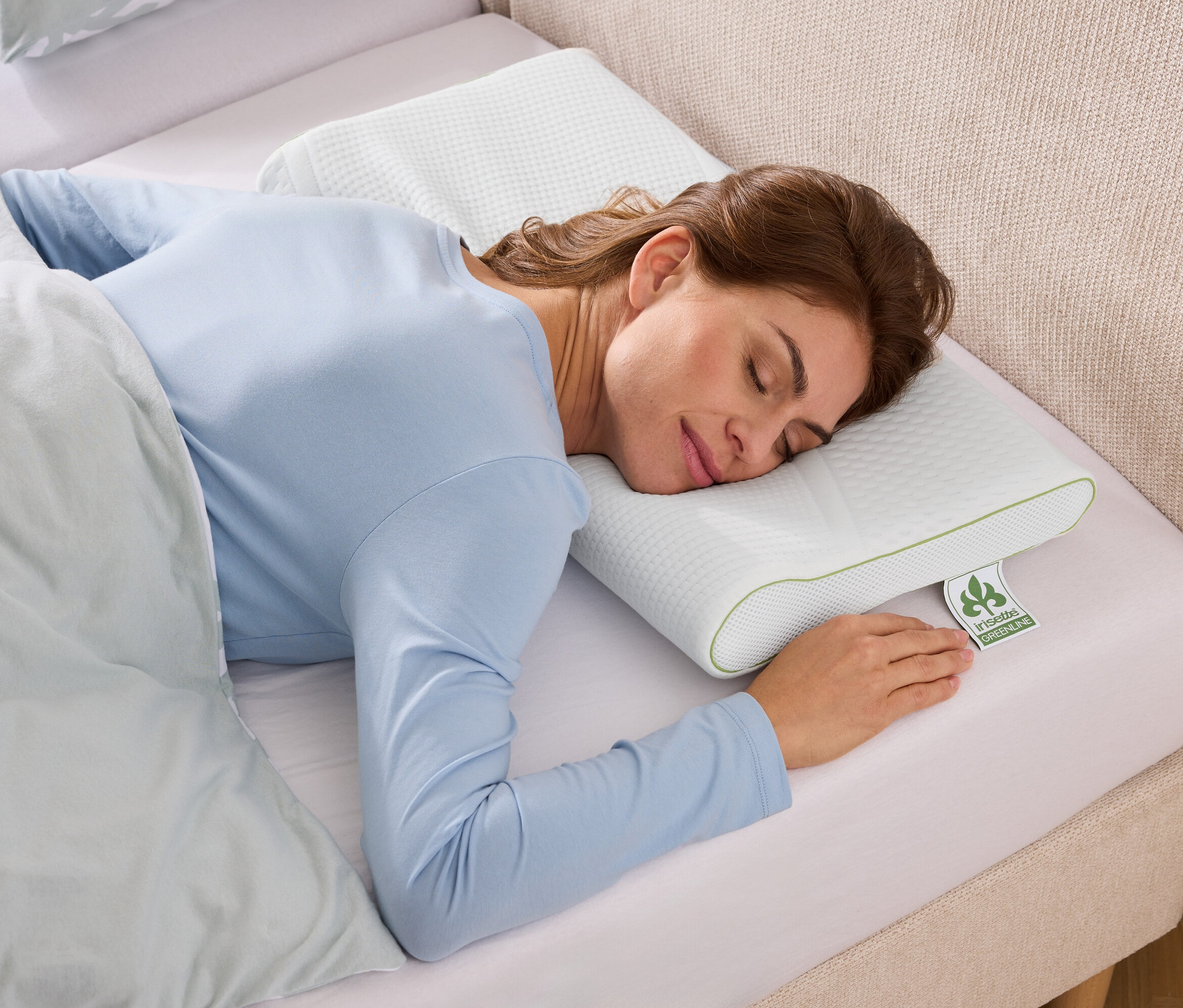 Nő alszik egy texturált, fehér párnán zöld díszítéssel egy világoskék ágyneművel ellátott ágyban.
