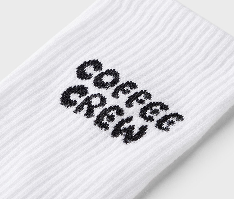 Közeli kép egy fehér zokniról, fekete "Coffee Crew" felirattal.