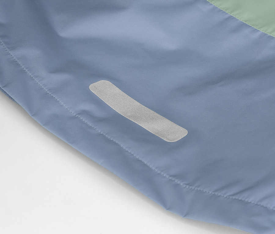 Egy kék-zöld kabát közeli képe, oldalán fényvisszaverő csíkkal.