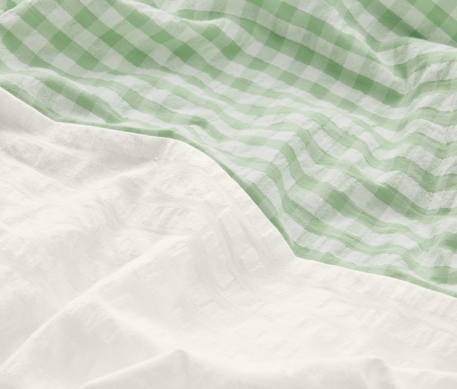 Közelkép a gyűrött ágyneműről: az egyik része fehér, a másik zöld-fehér kockás.