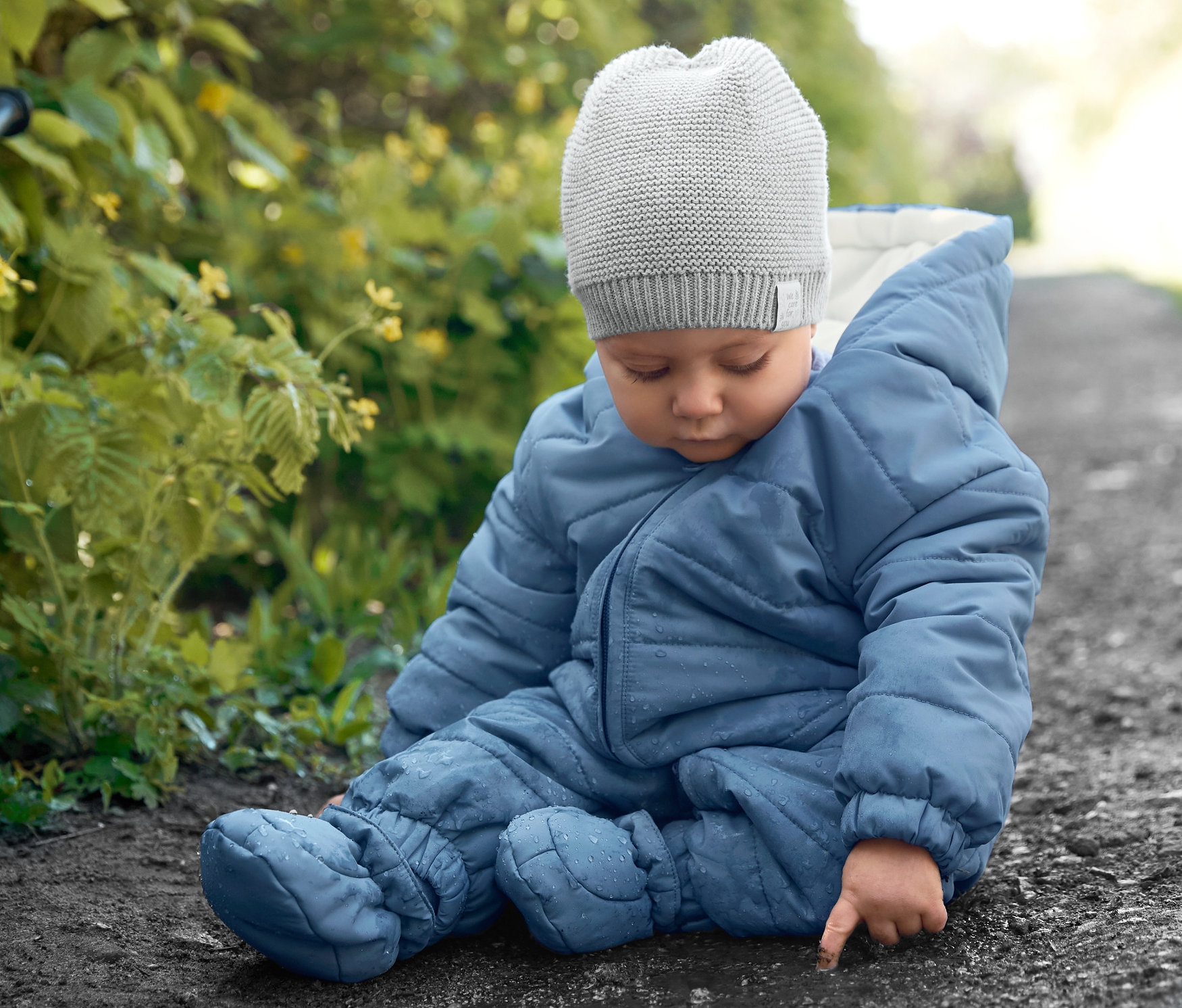 Baba ül a földön kék téli overallban és kötött sapkában.