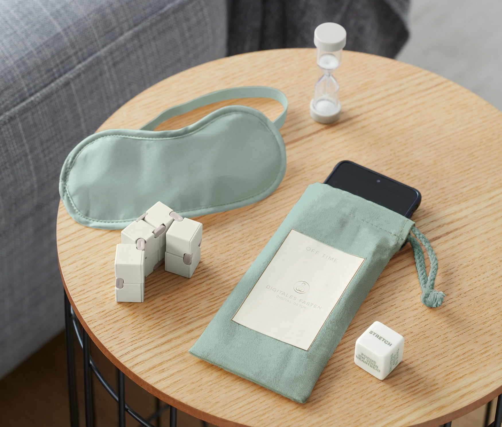 Egy asztalon digitális detox készlet, szemmaszk, homokóra és kocka.