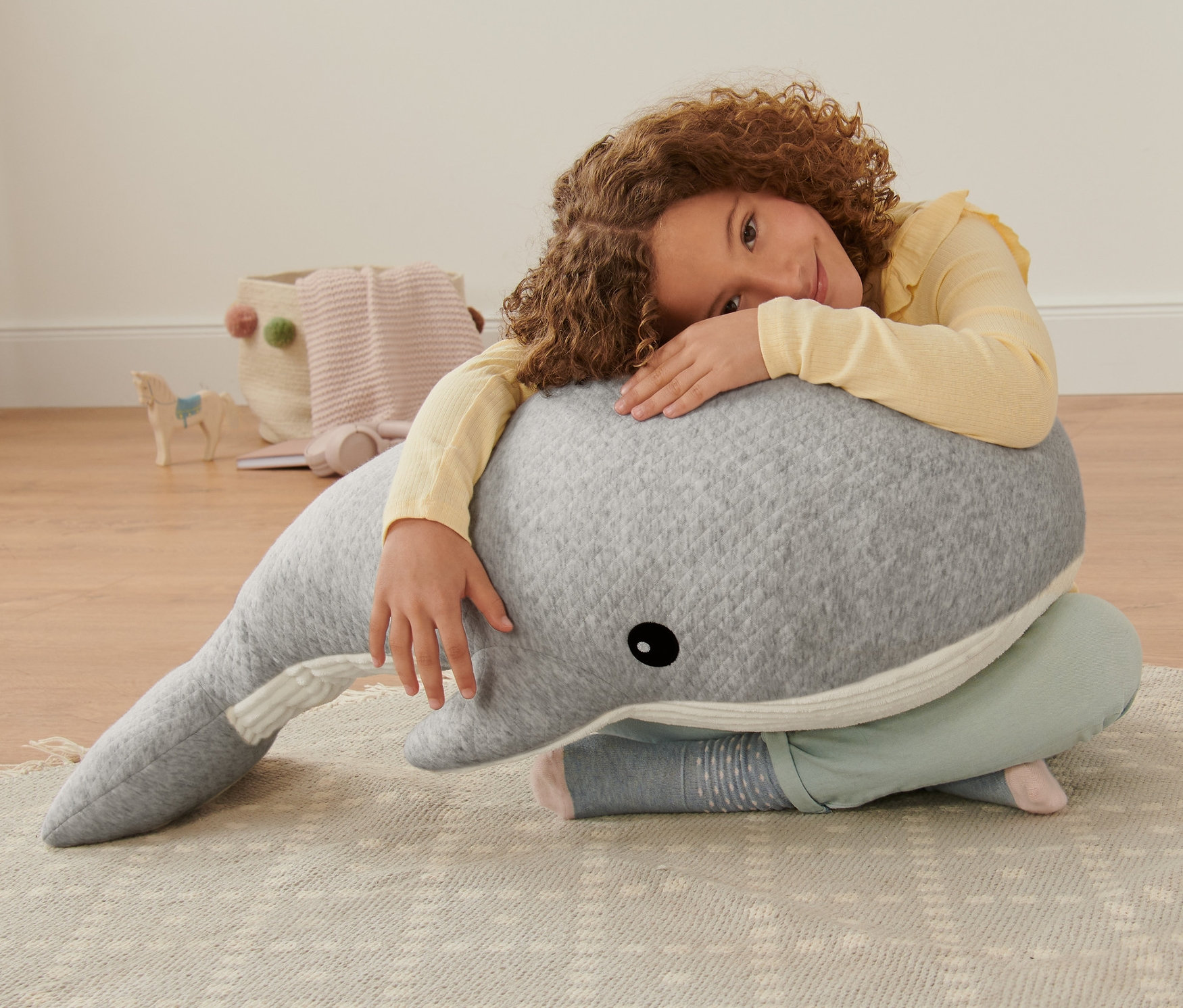 Egy lány ölel egy óriás plüss bálnát.