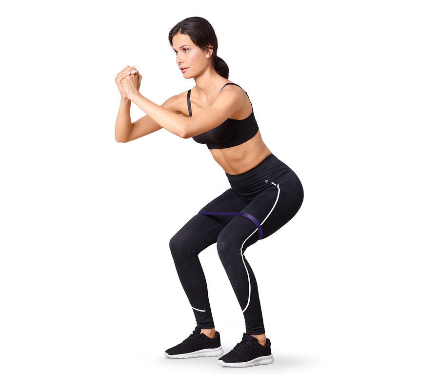 Nő fekete sportmelltartóban és leggingsben guggolást végez lila fitneszszalaggal. 2 fitneszszalag és 2 gumiszalag.