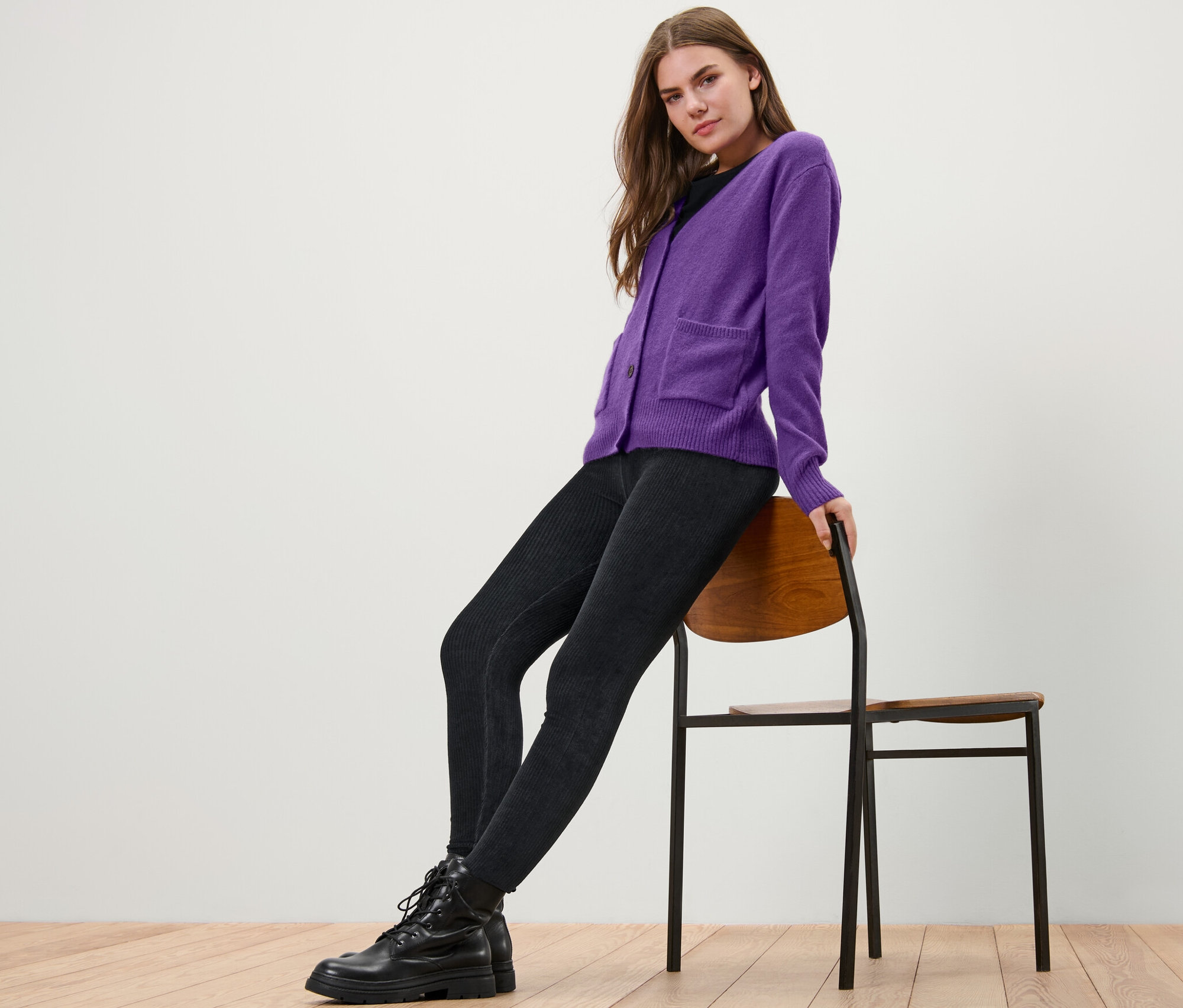 Nő ül egy széken, lila, gyapjú kötött kardigánt visel.