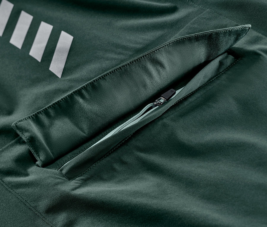 Egy sötétzöld női kerékpáros esőkabát részlete, ezüst csíkokkal és cipzáras zsebbel.