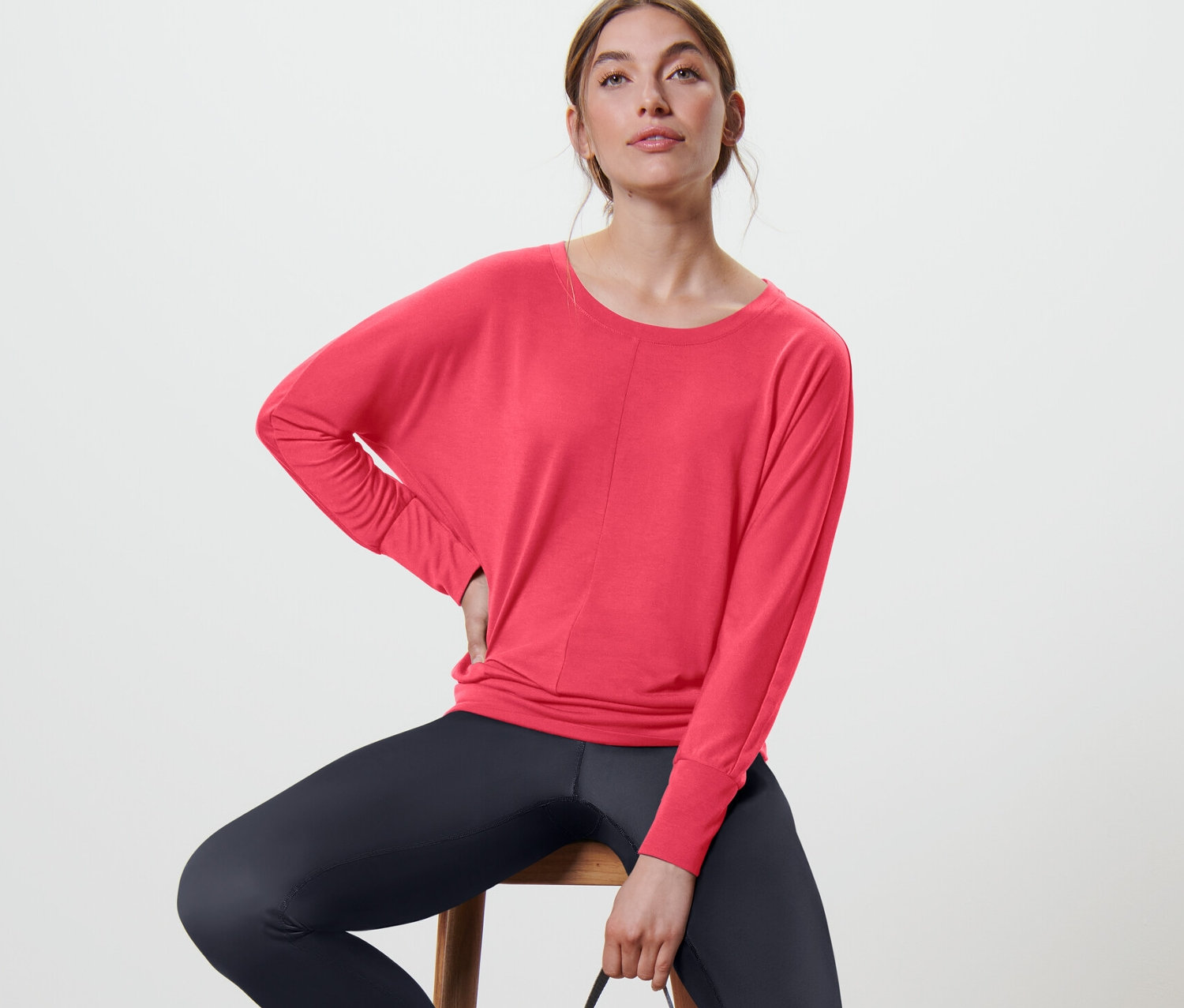 Nő ül egy széken, és rózsaszín női denevérujjú sportfelsőt visel.