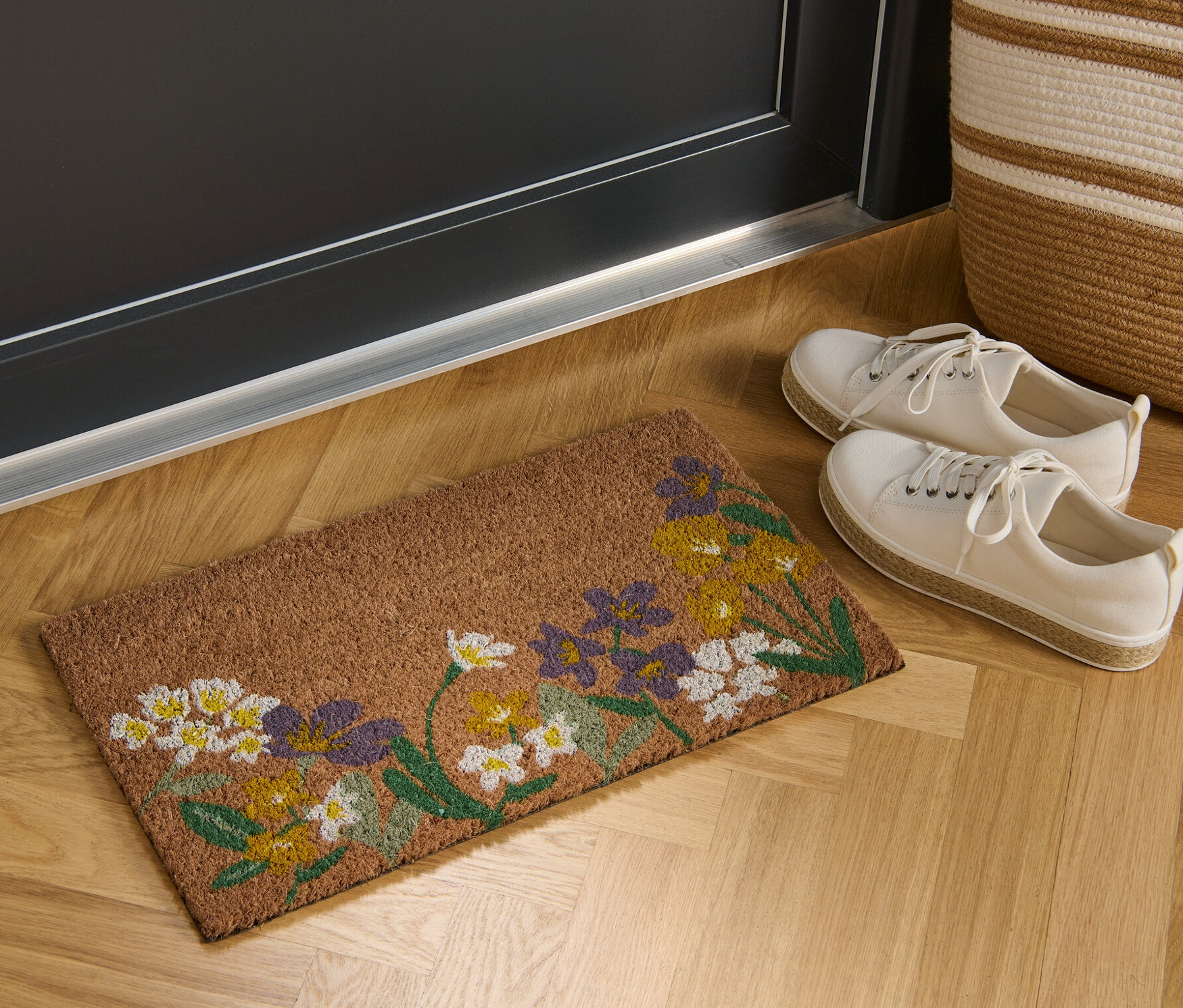 Egy virágmintás kókusz lábtörlő fekszik egy ajtó előtt.