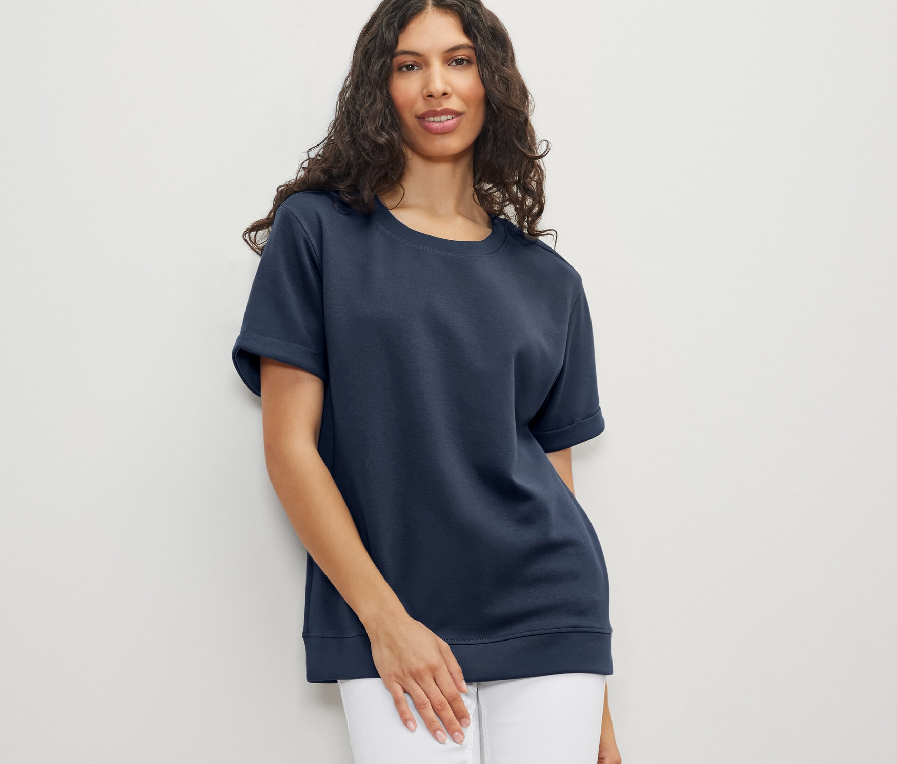 Nő visel sötétkék női felsőt és fehér farmert.