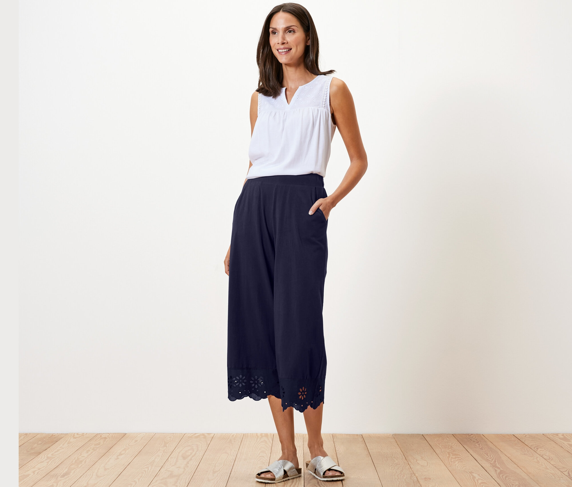 Nő pózol fehér felsőben és sötétkék, hímzett culotte nadrágban.