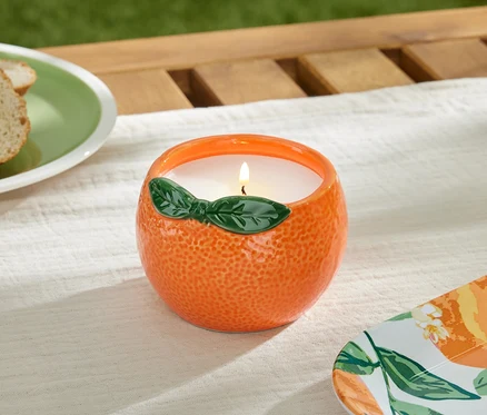 Égő citronella gyertya narancs alakú tálban az asztalon.
