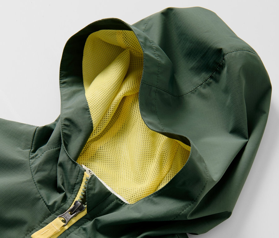 Egy zöld, kapucnis, sárga cipzáras gyerek sportdzseki részlete.