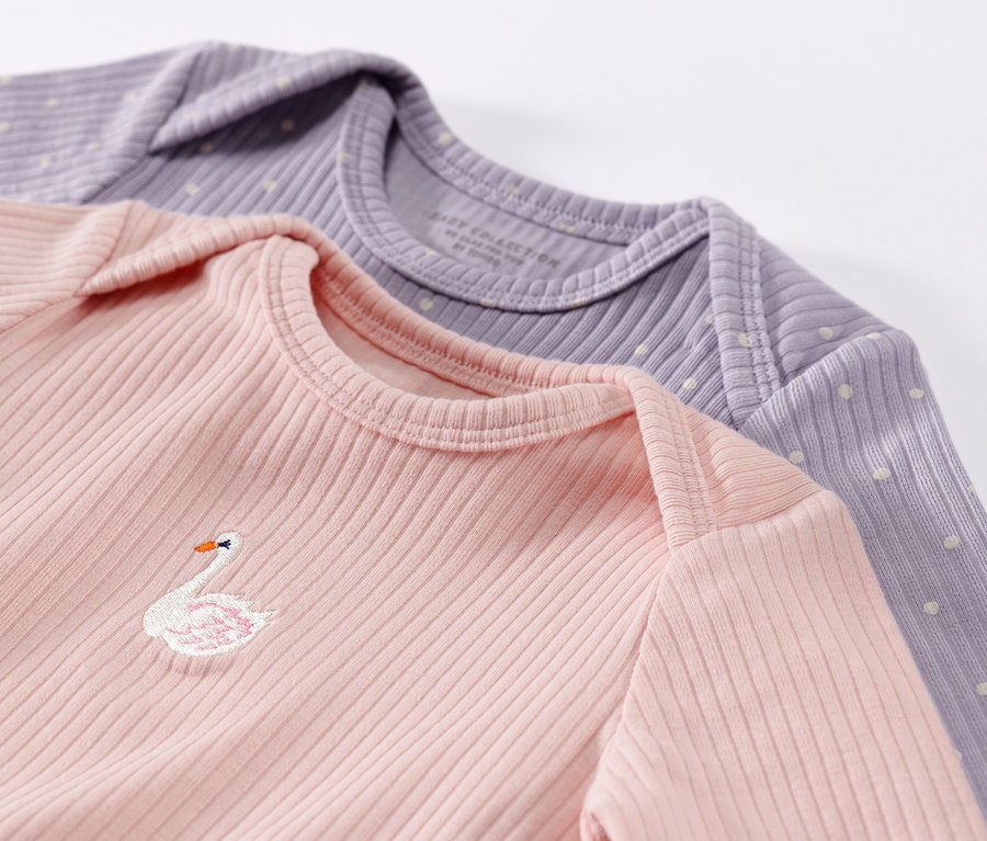 Két hosszú ujjú, bordázott kisgyermek felső közeli képe rózsaszínben és lilában. A rózsaszín felsőn egy hattyú hímzés található.