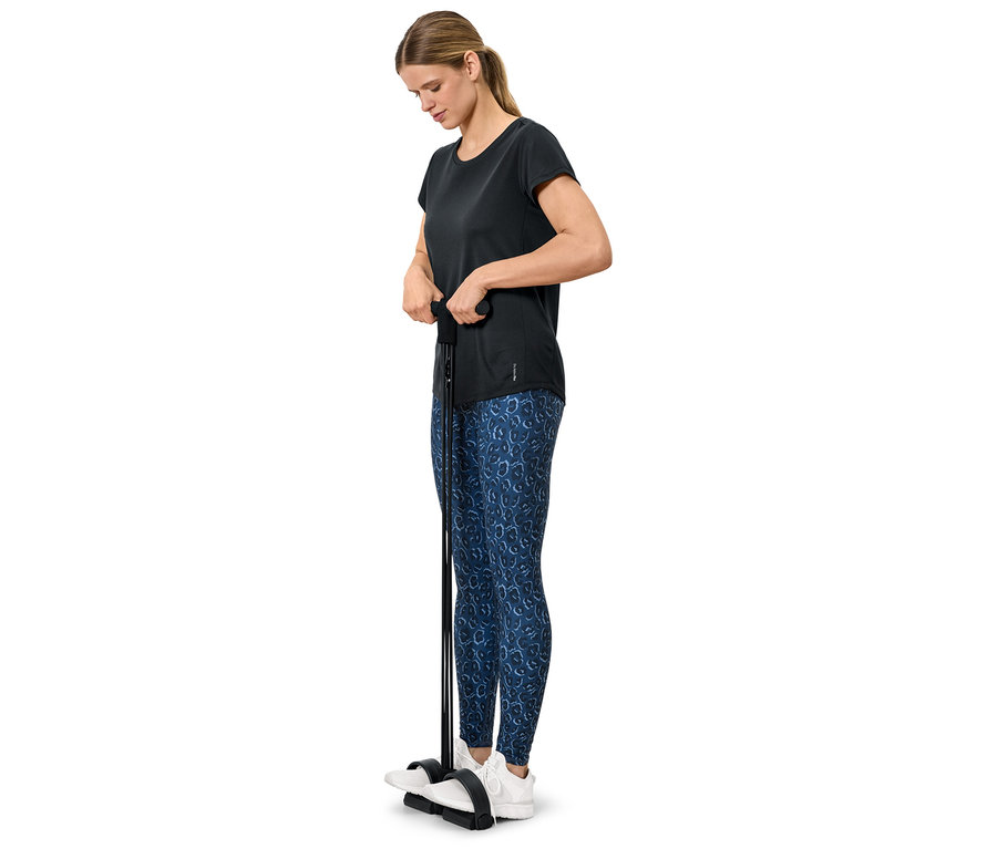 Nő edz egy fitneszgéppel, fekete pólót és kék leggingst visel.
