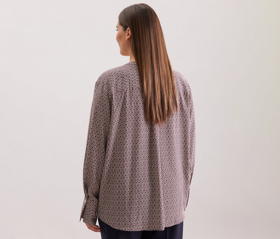 Hátulnézet egy hosszú barna hajú nőről, aki egy ekrü-bordó mintás Seidensticker viszkóz tunikát visel.