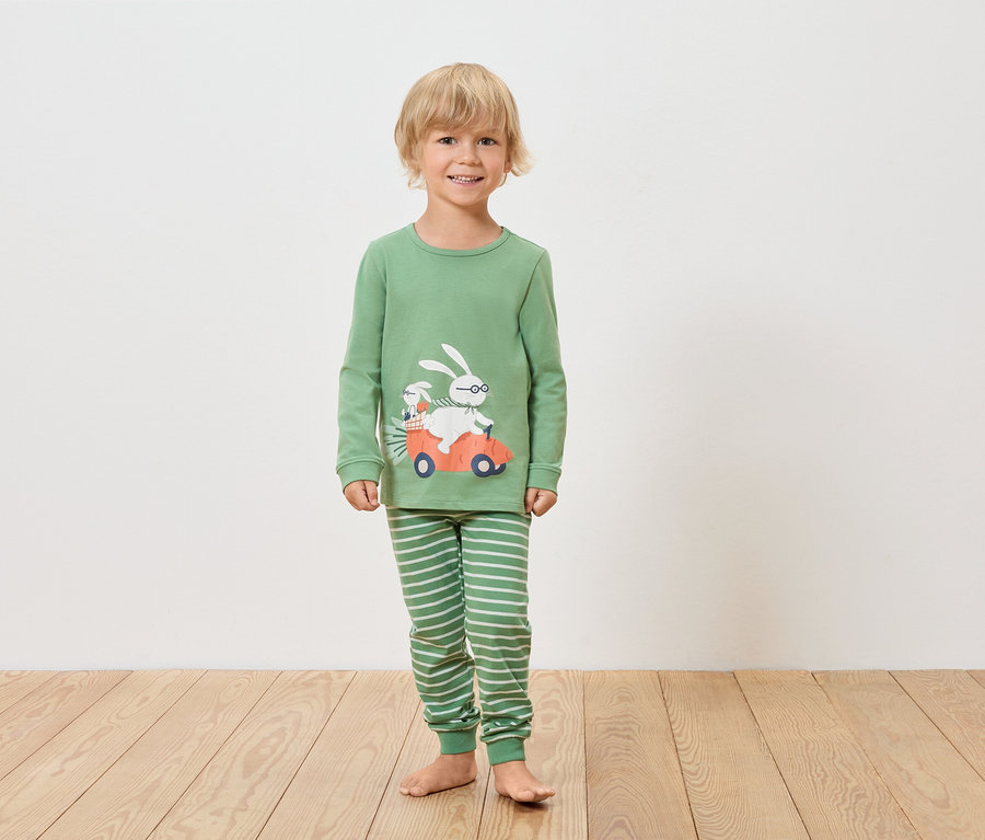 Egy fiú zöld, hosszú ujjú pizsamát és csíkos nadrágot visel, nyuszi mintával egy autóban.