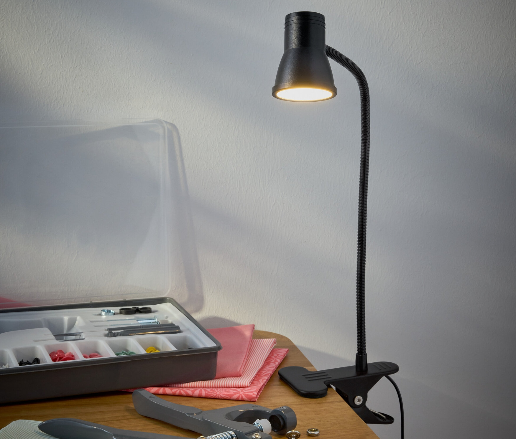 Egy fekete LED-es csíptetős lámpa áll az asztalon egy varrókészlet mellett.