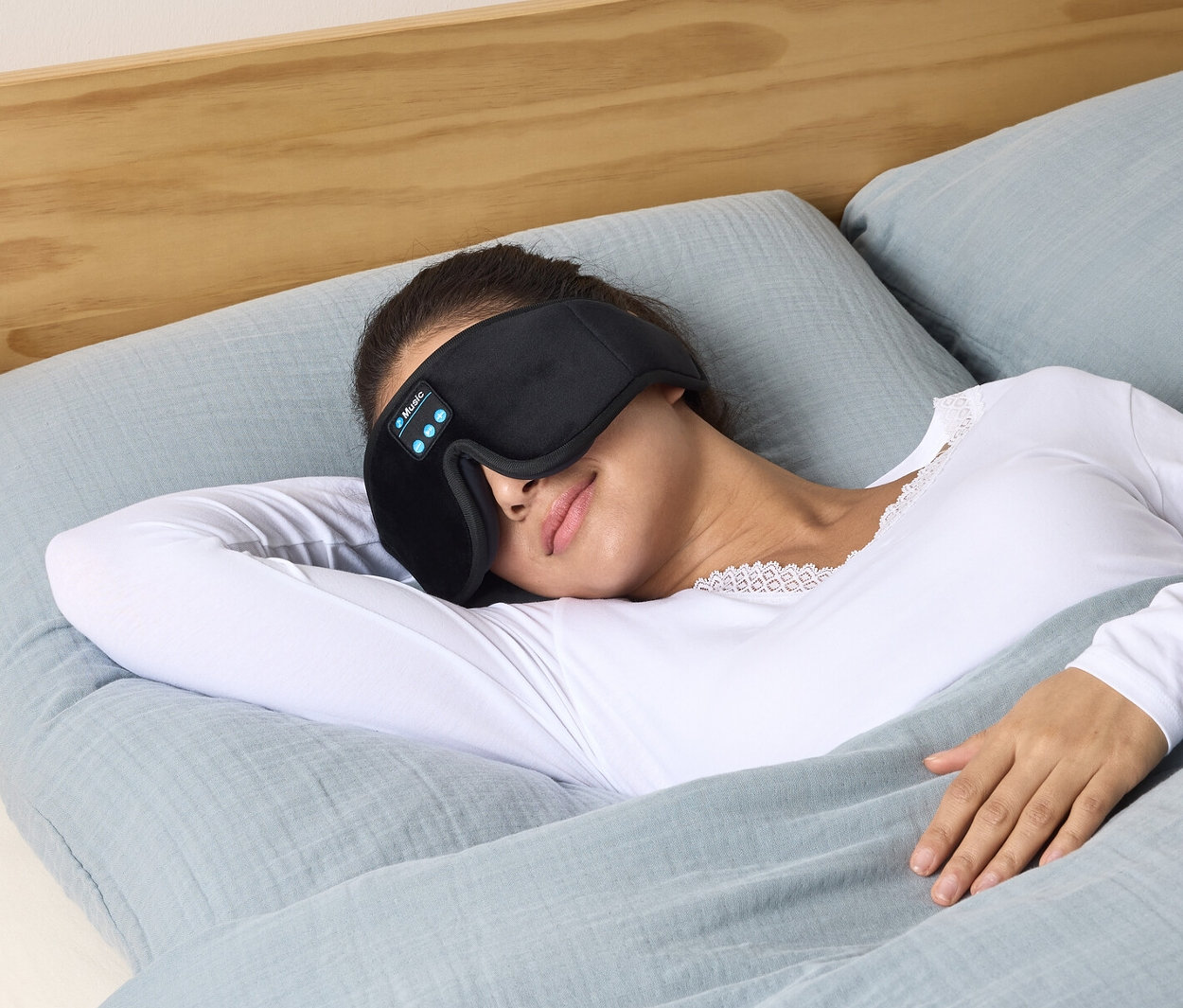 Nő fekszik az ágyban, alvómaszkot visel fülhallgatóval.