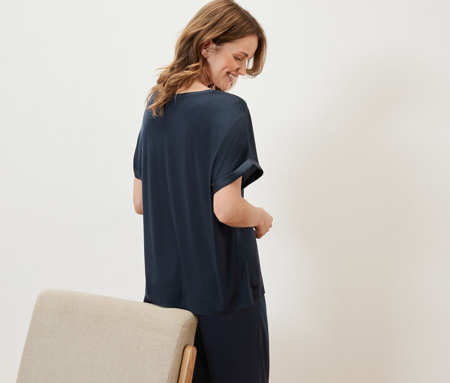 Nő lefelé néz, tengerészkék ingblúzt és sötétkék nadrágot visel.