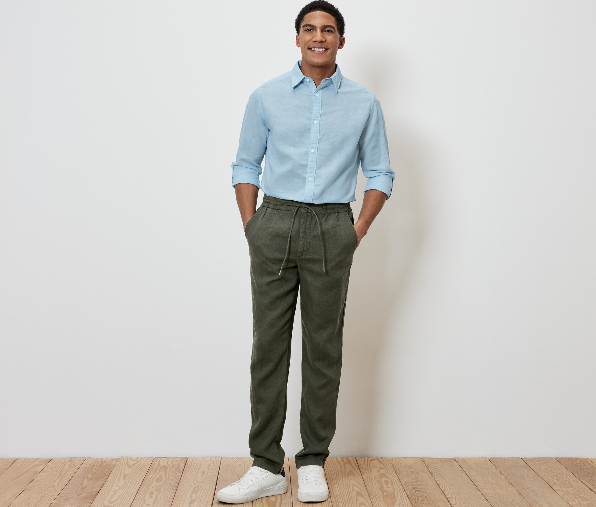 Egy férfi áll, kezét a khaki lenvászon chino nadrág zsebébe dugva.