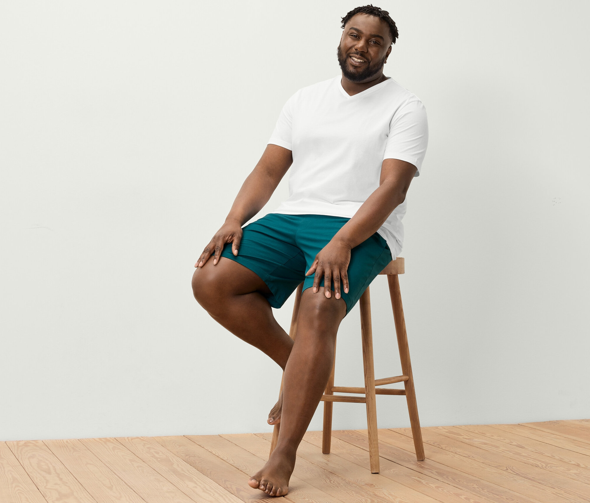 Egy férfi ül egy széken, fehér V-nyakú pólót és szabadidő rövidnadrágot visel.