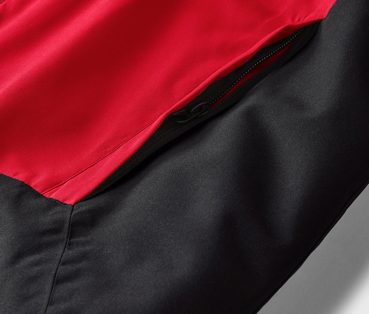 Egy piros-fekete dzseki részlete, zsebbel és cipzárral.