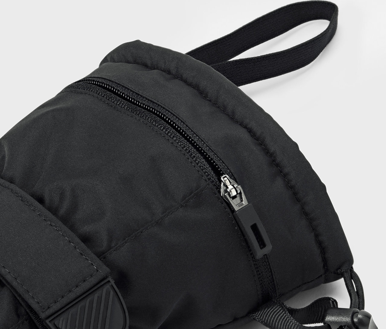 Egy fekete hátizsák részlete, látható cipzárral és pánttal.