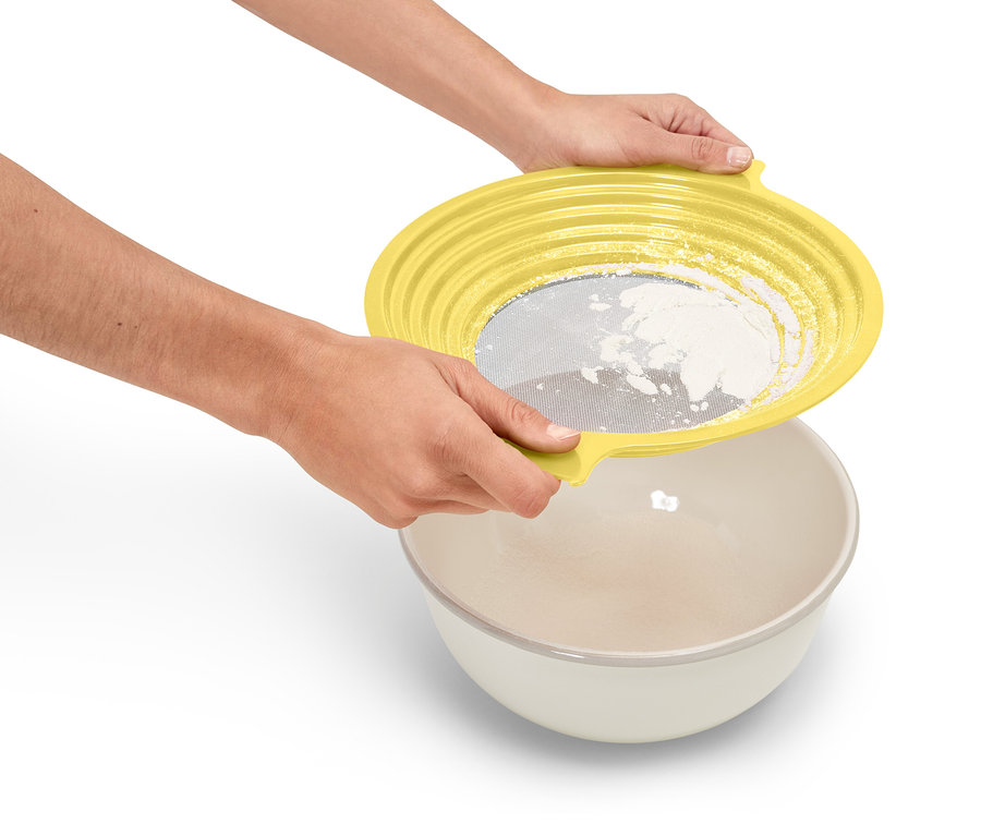 Egy személy sárga szitát tart egy tál fölé, és lisztet szitál.