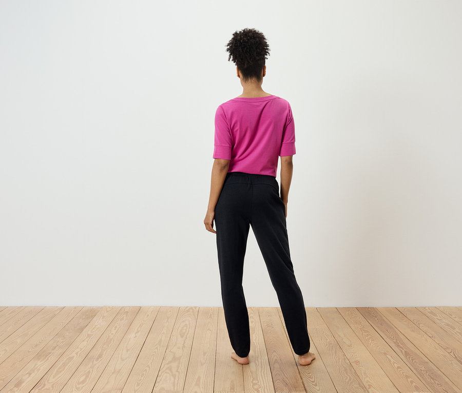 A kamerának háttal álló nő rózsaszín pólót és fekete nadrágot visel.