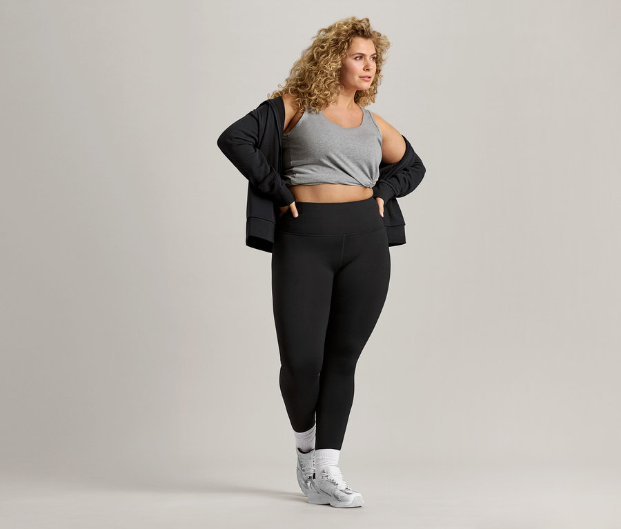 A göndör hajú nő szürke trikót, fekete kabátot és fekete leggingset visel.