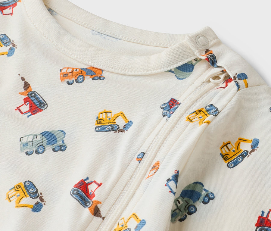 Krémszínű, cipzáras babaruha közelképe építőipari teherautó mintával.