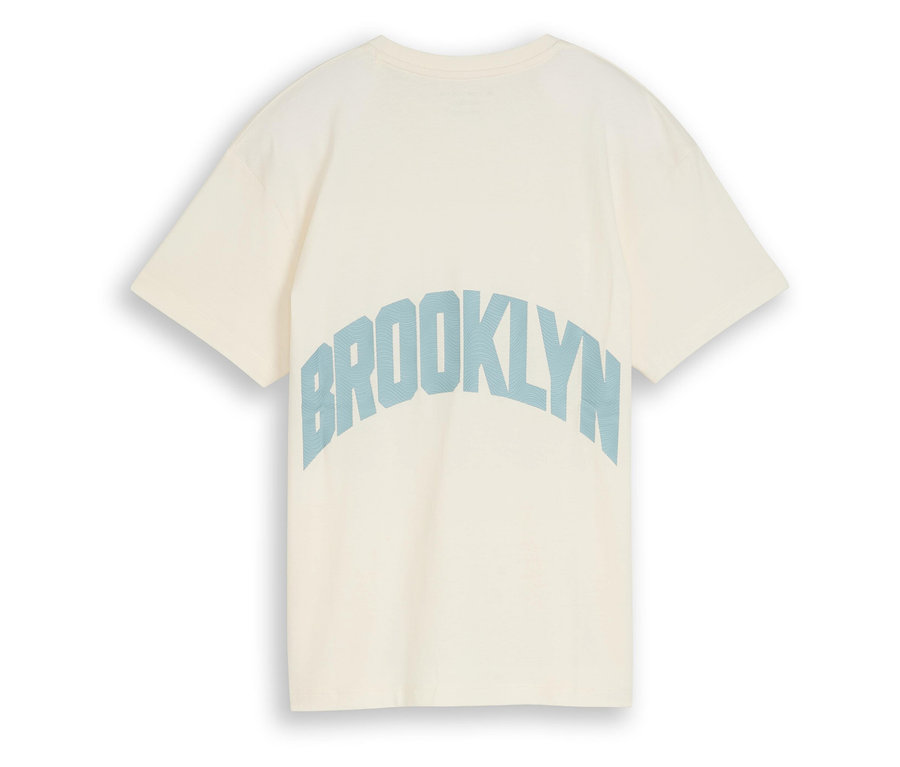 Krémszínű póló közeli képe, hátulján kék "Brooklyn" felirattal.