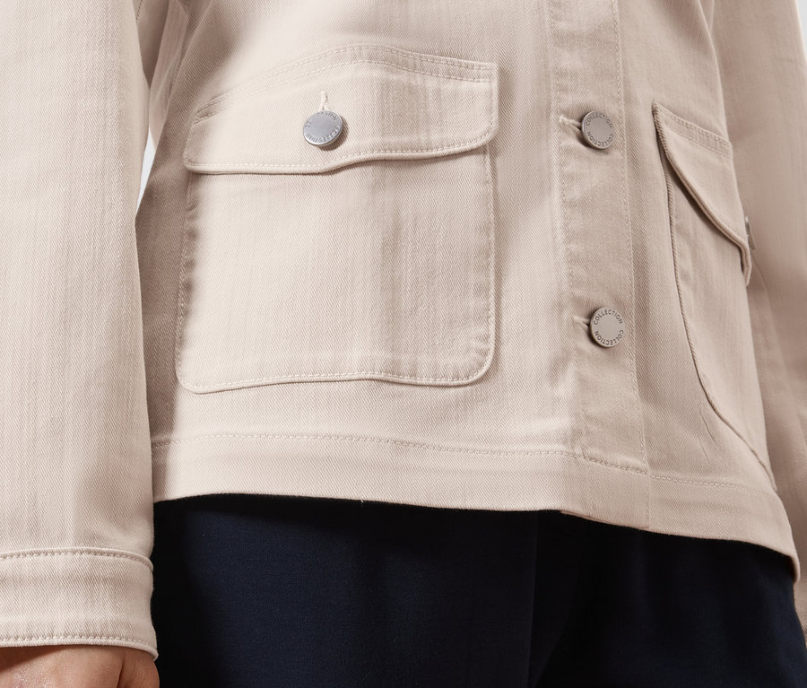 Közeli kép egy világosbarna farmerdzsekiről ezüst gombokkal és rávarrt zsebekkel.