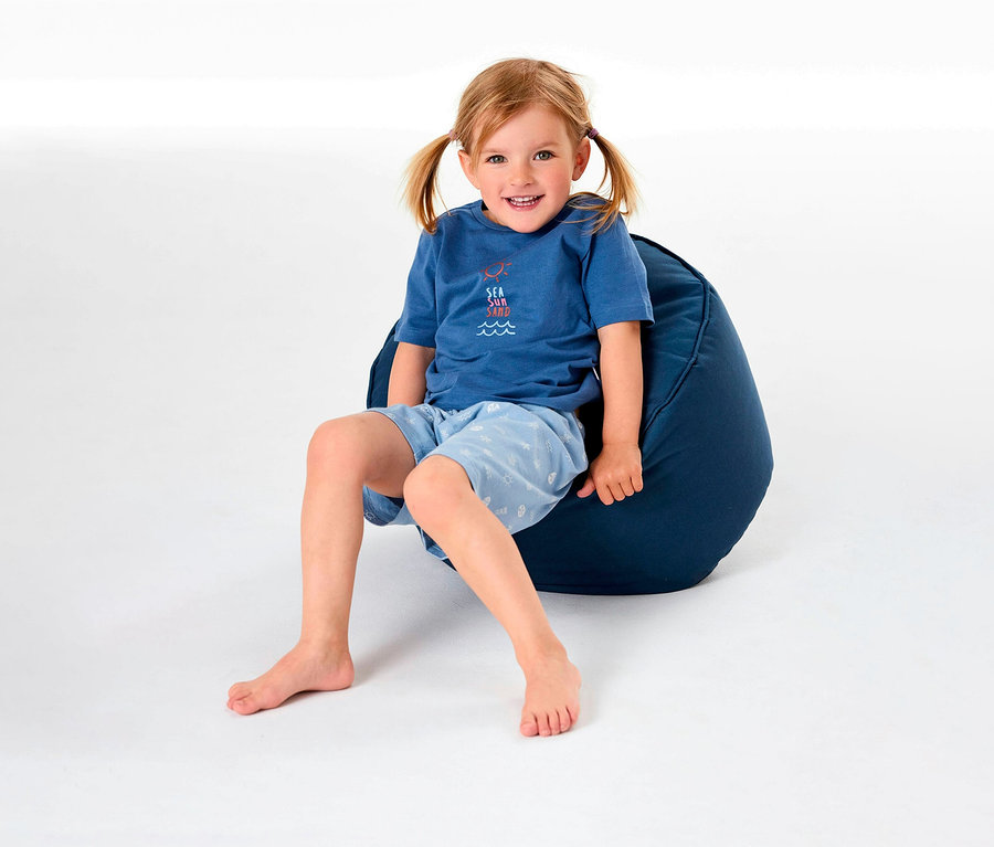 Egy kislány ül egy babzsákon, és SCHIESSER rövidnadrágos gyerekpizsamát visel.