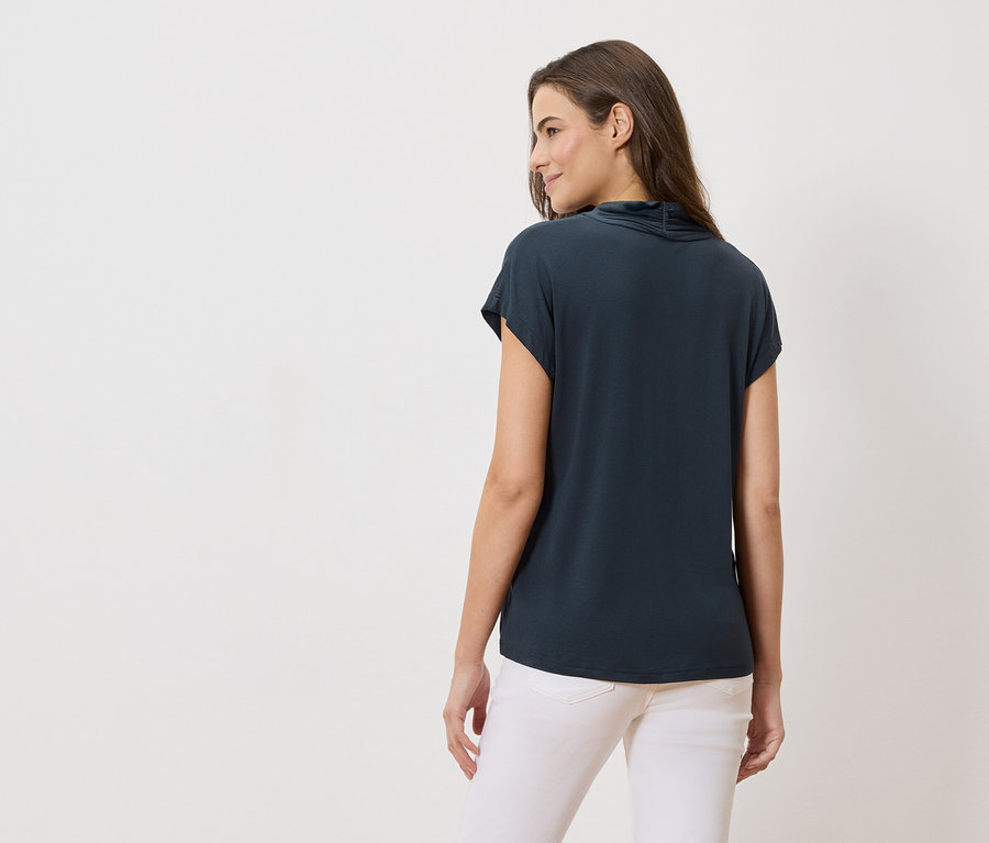 Hátulnézet egy hosszú, barna hajú nőről, aki tengerészkék felsőt és fehér farmert visel.