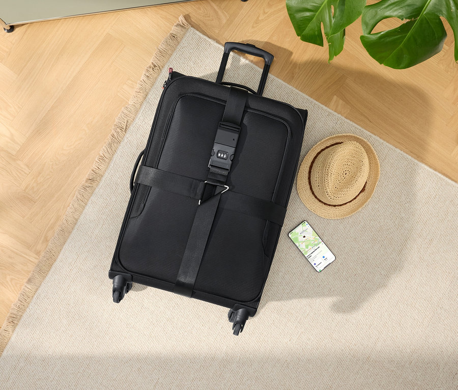 Fekete gurulós bőrönd kalappal és okostelefonnal egy bézs szőnyegen.