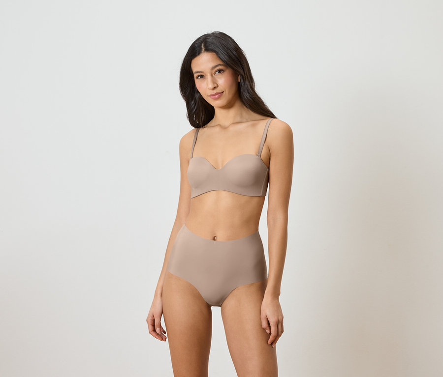 Nő visel bézs színű, pánt nélküli melltartót és magas derekú alsót.