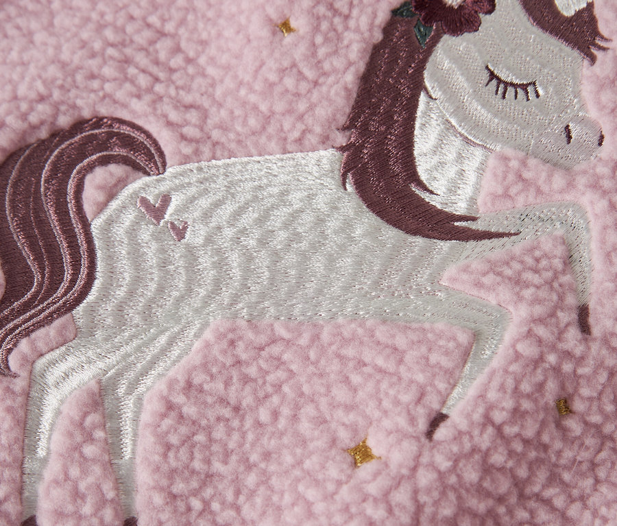 Egy rózsaszín polár anyag közelképe, hímzett unikornis applikációval.
